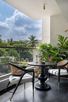 two chairs and a table on a balcony overlooking the trees in the distance, with plants growing out of them