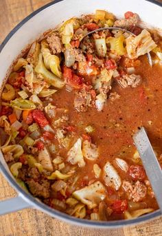 a large pot filled with meat and vegetable soup on top of a wooden table next to a spoon