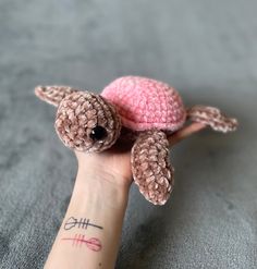 a small stuffed turtle sitting on top of a person's hand with a tattoo