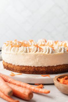 a carrot cake with whipped cream on top and sliced carrots next to the cake