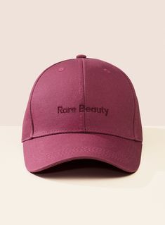 a pink baseball cap with the words rare beauty printed on it, sitting on a white surface