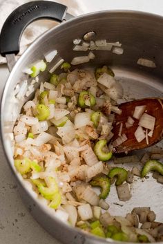 onions and celery being cooked in a pot with a wooden spoon on the side