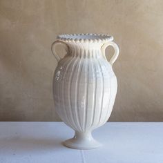 a white vase sitting on top of a table next to a beige wall and floor