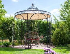 a gazebo sitting in the middle of a lush green yard with flowers around it