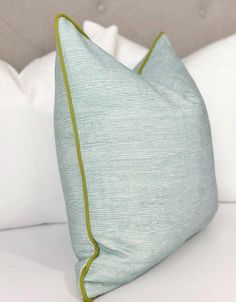 a bed with white pillows and green trimmings on the pillowcase, along with a gray headboard