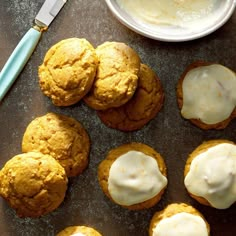 several cookies with white icing on a baking sheet next to a bowl of cream cheese