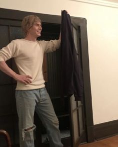 a man standing in front of a closet holding onto a black coat hanging from it