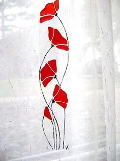 red flowers are on the window sill in front of white sheer curtains and drapes