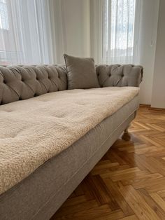 a couch sitting on top of a hard wood floor next to a window with white curtains