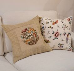 two pillows are sitting on the back of a white couch with floral designs and birds