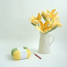 yellow flowers in a white vase next to a ball of yarn