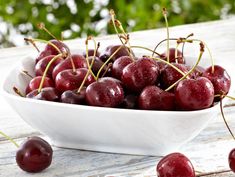 a white bowl filled with cherries on top of a wooden table