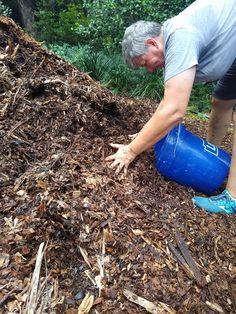 a man is picking up some mulch from the ground with a blue plastic bucket