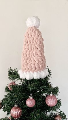 a crocheted hat on top of a christmas tree with ornaments around the base