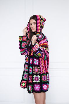 a woman in a colorful crochet coat is posing for the camera with her hand on her hip