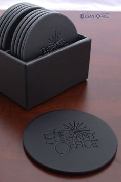 a stack of black plates sitting on top of a wooden table next to a coaster