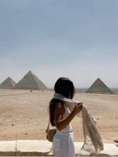 a woman standing in front of three pyramids with a scarf around her neck and wearing a white dress