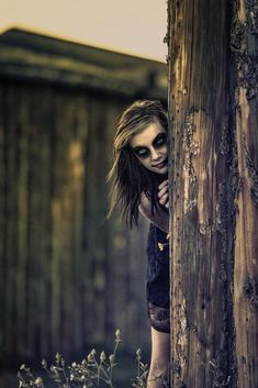 a woman with makeup on her face leaning against a wooden pole in front of a fence