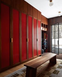 a wooden bench sitting in the middle of a room next to red cupboards and doors