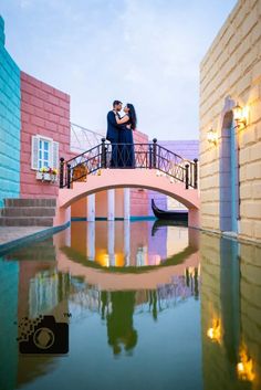 a man and woman standing on a bridge over a body of water with a gondola in the background