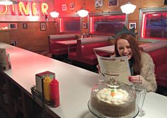 a woman sitting at a table with a cake in front of her reading a menu