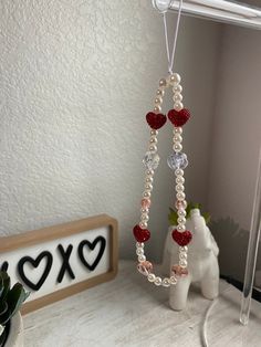 a heart shaped beaded necklace hanging from a hook on a shelf next to a vase