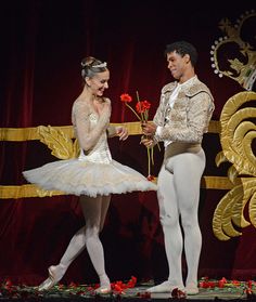 two ballerinas in white tutus standing on stage with one holding a rose