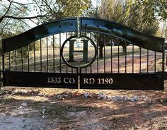 an iron gate with a plaque on it in front of a dirt field and trees