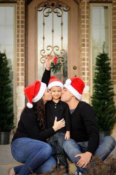 a man and woman kissing while holding a child in front of a house with christmas decorations