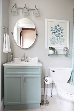 a white toilet sitting next to a bathroom sink under a round mirror on a wall