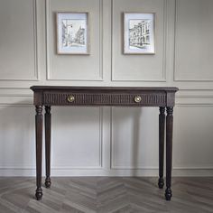 a wooden table with two pictures on the wall behind it in a room that has wood flooring and white walls