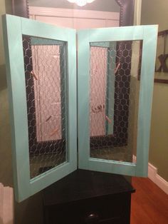 an open blue cabinet with chicken wire on the top and bottom, in front of a mirror