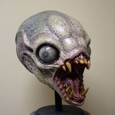 an alien head with large teeth and sharp fangs on top of a wooden table next to a white wall