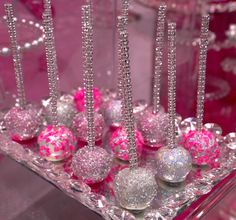 there are many pink and silver balls in the glass tray on the table with candles