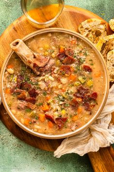 a bowl of soup with meat and vegetables on a wooden platter next to bread