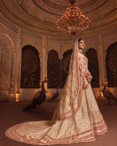 a woman in a bridal gown standing next to peacocks and chandelier