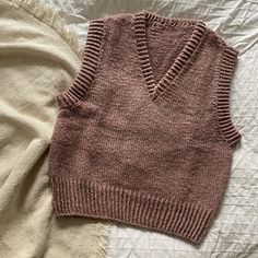 a pink sweater vest laying on top of a bed