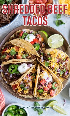 shredded beef tacos on a plate with limes, tomatoes and cilantro