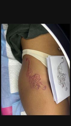 a woman's stomach with a tiger tattoo on it and a book laying next to her