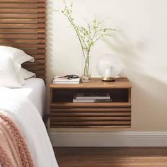 a bed with white sheets and pillows next to a wooden night stand on top of a hard wood floor