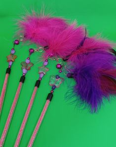 four pink and purple feathers on top of each other next to two pens with beads