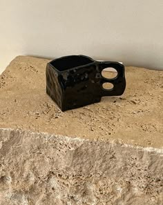 a small black vase sitting on top of a stone slab next to a white wall