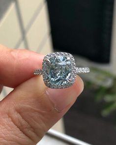 a close up of a person's hand holding a ring with a blue diamond