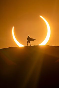 a man holding a surfboard standing on top of a hill with the moon in the background