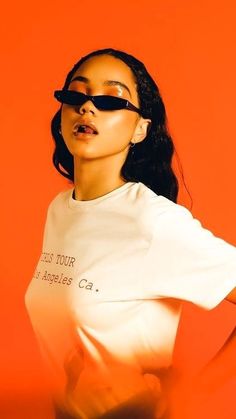 a woman wearing sunglasses standing in front of an orange background