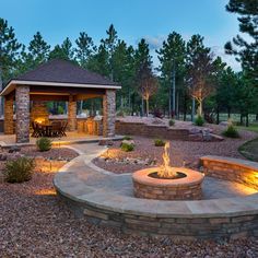 an outdoor fire pit surrounded by rocks and landscaping lighting up the landscape at night time