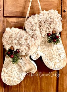 two white christmas stockings hanging on a wooden door with holly berries and pine cones attached to them