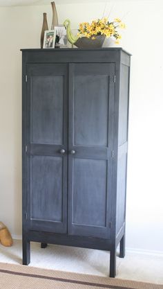 a black armoire sitting on top of a rug next to a vase with flowers