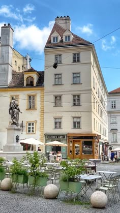 there are many tables and chairs on the street in front of this building with people walking by