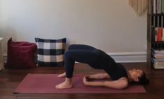 a woman in black shirt doing yoga on pink mat next to bookshelf and couch